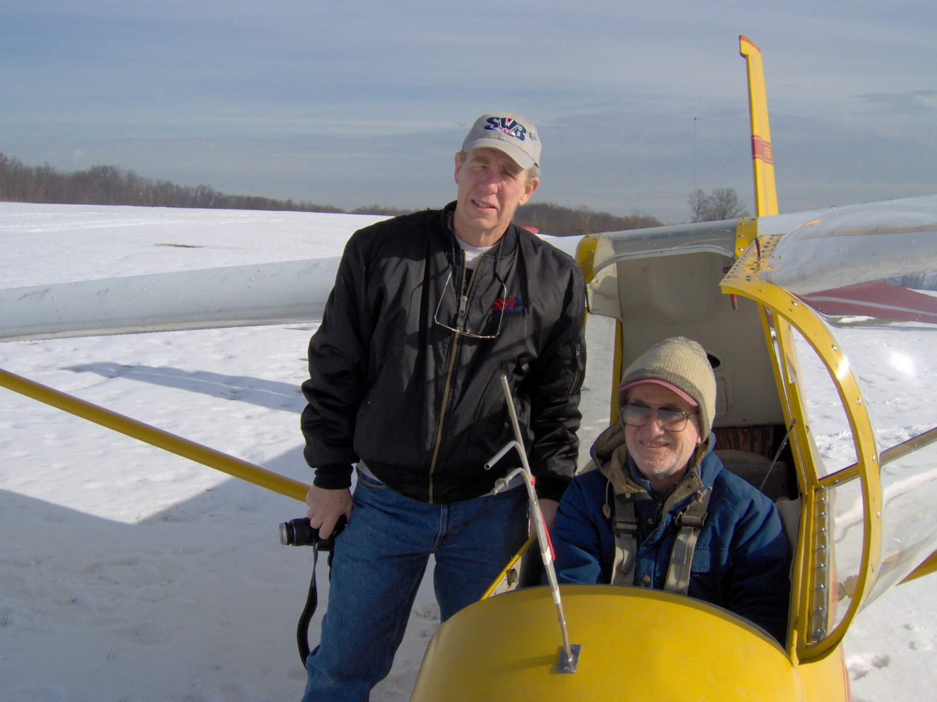 Stephen H. Unger sits in his plane on snowy ground, posing with another individual