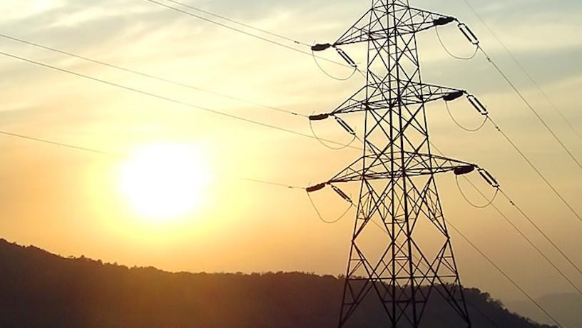 an electrical tower with wires attached stands with the sun in the background